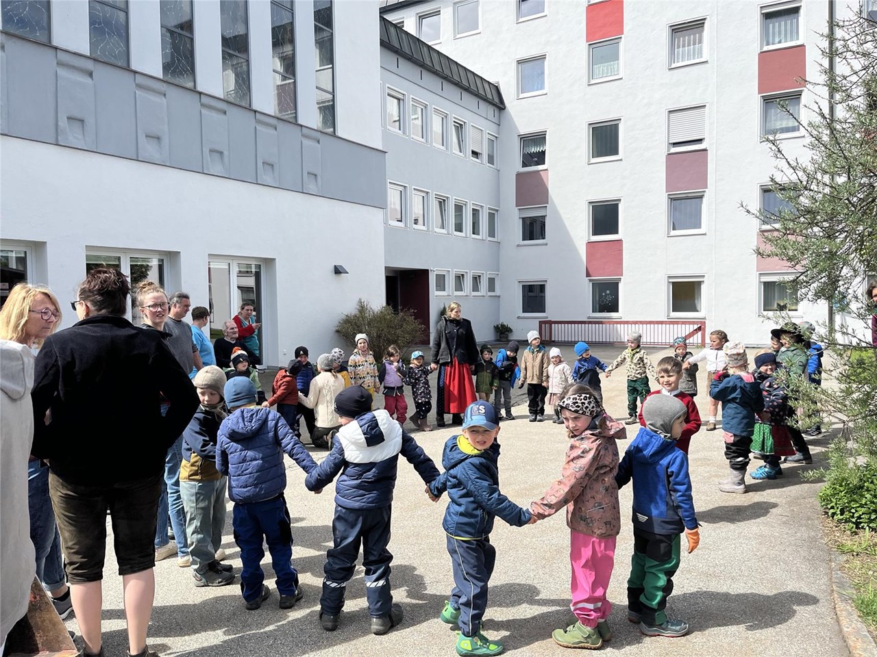 Kinder des Waldkindergartens Freyung tanzen beim Maifest im Garten des Caritas-Seniorenheims St. Gunther, während Senioren und Mitarbeitende zusehen.
